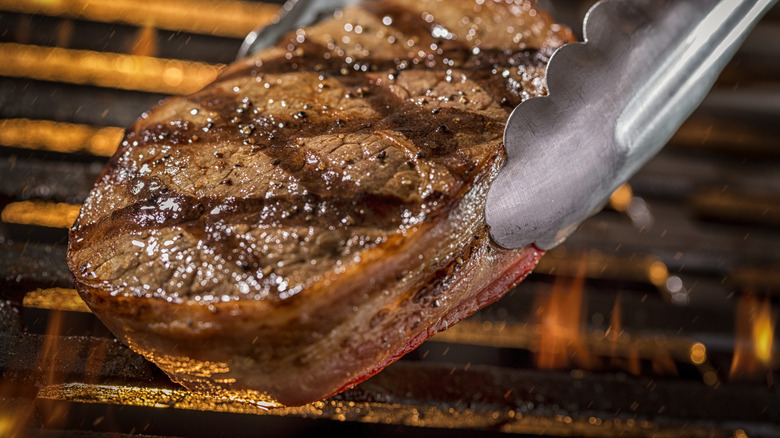 Tongs flipping steak over on grill