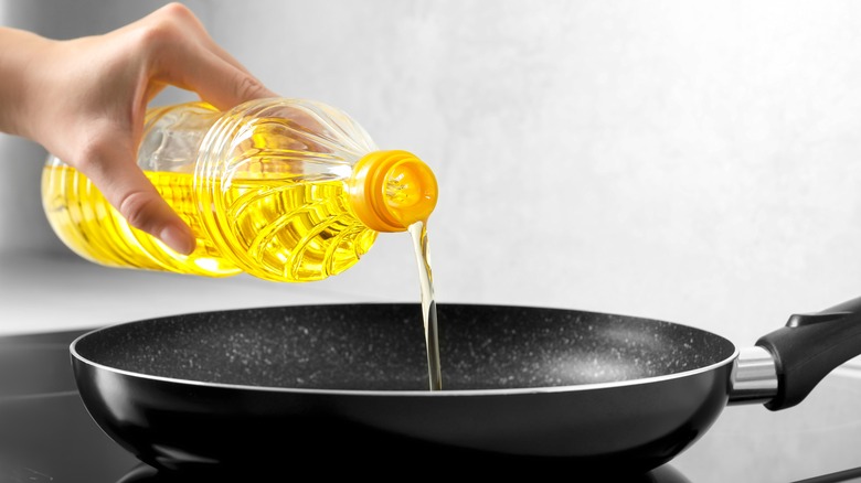 Hand pouring cooking oil into a pan