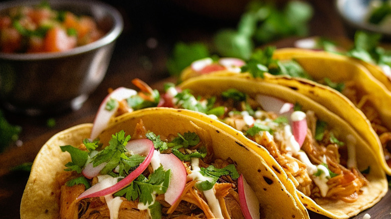 Row of shredded chicken tacos with fresh toppings