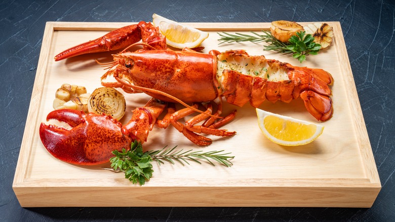 Grilled lobster on wooden plate with lemon wedges