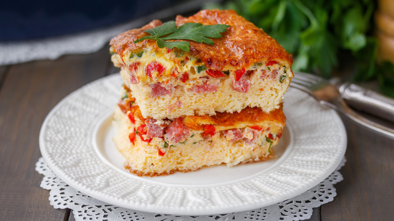 Fluffy slices of Spanish omelet with ham and veggies stacked on plate