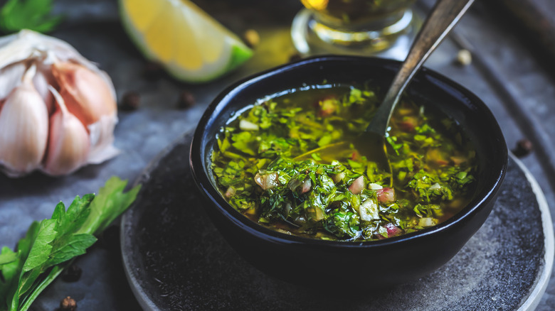 Chimichurri in bowl with spoon and garlic