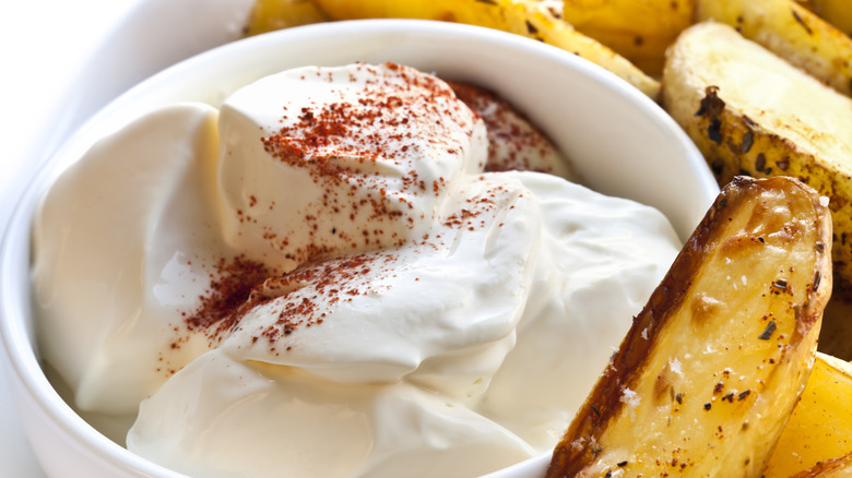 Sour cream in bowl with potato wedges