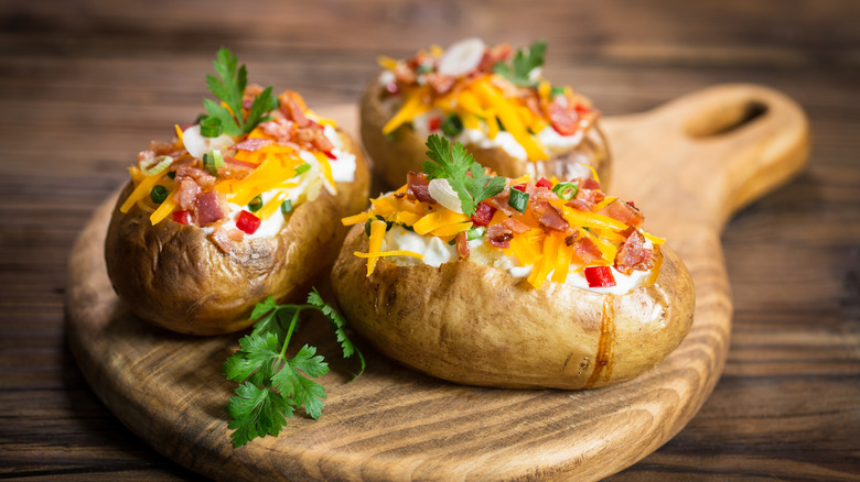 baked potatoes on wood board with cheese, sour cream and bacon