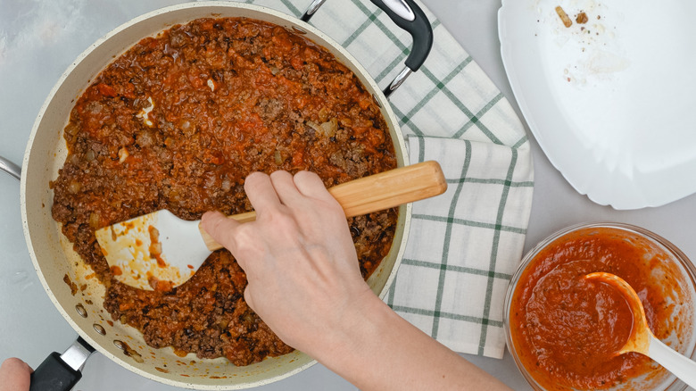 Hand mixing ground beef and tomato sauce together in pan