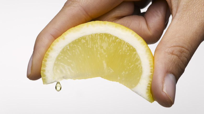 Hand squeezing slice of lemon