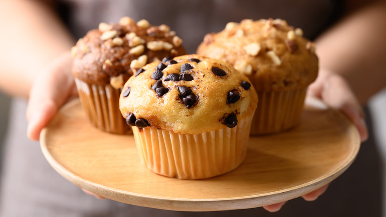 Hands holding plate of assorted muffins