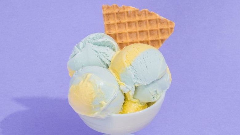 hand holding a waffle cone of yellow and blue ice cream