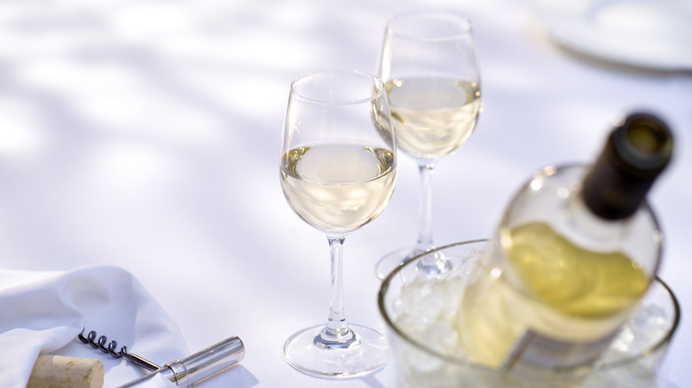 a white wine bottle in an ice bucket next to two filled wine glasses