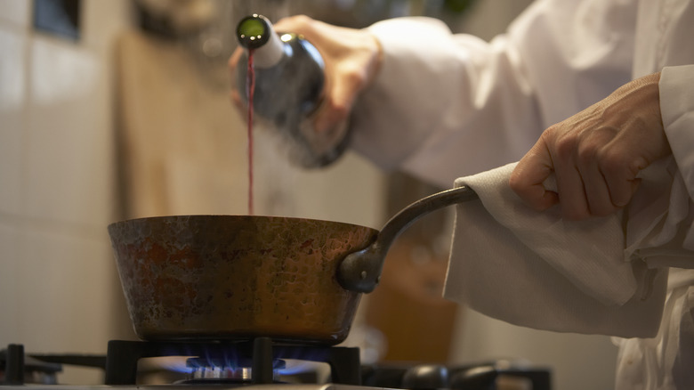 person pouring wine into saucepan