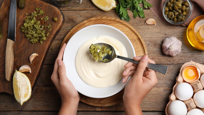 person adding pickles to mayonnaise