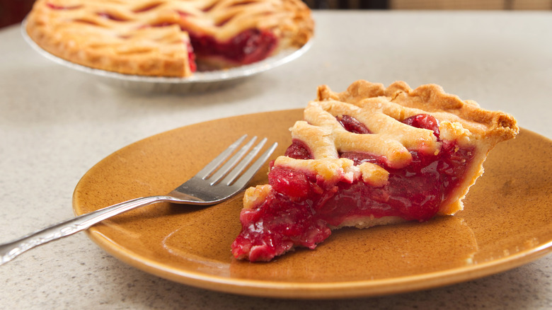 Slice of cherry pie on orange plate with fork