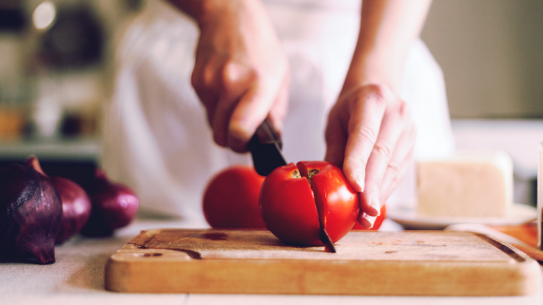 Hands slicing tomatoes and onions 