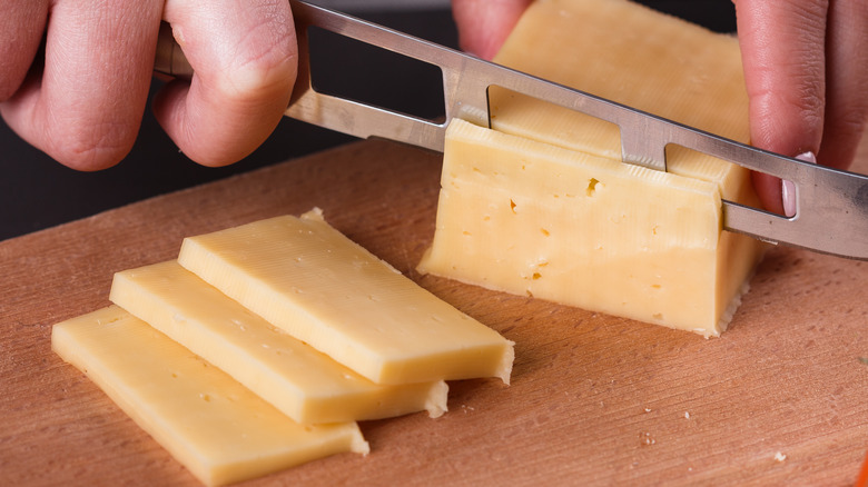 Hands slicing block of cheese
