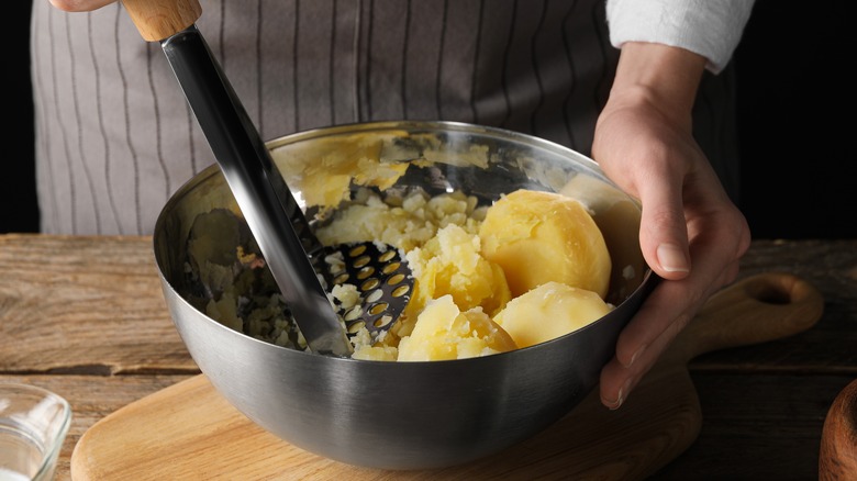 chef mashing potatoes in bowl