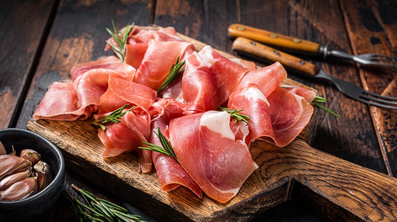 Sliced prosciutto and rosemary sprigs on a wooden board
