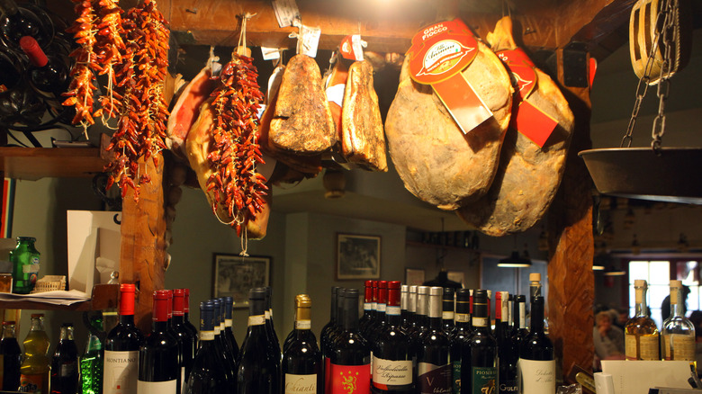 Whole prosciutto hanging from ceiling over wine bottles
