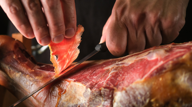Closeup of prosciutto being sliced off whole leg