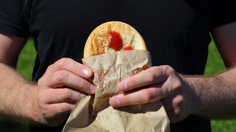 man holding meat pie in paper bag