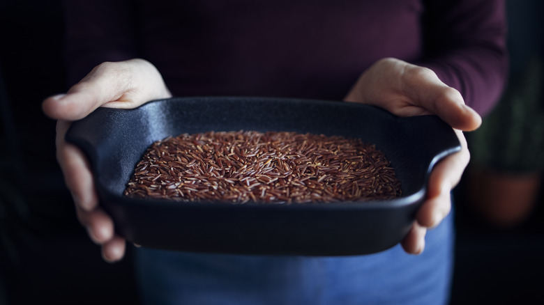 Hands holding a metal pan of red rice
