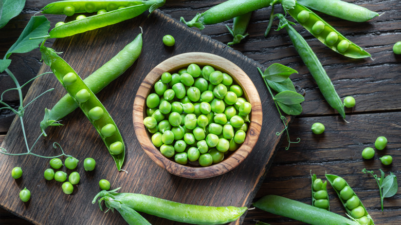 Bowl of peas surrounded by pea pods