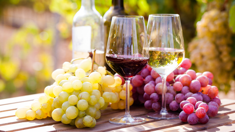 Two glasses of red and white wine next to red and white grapes