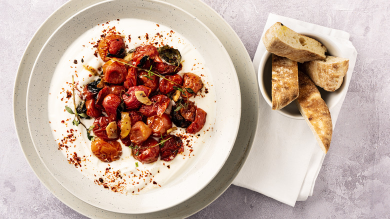 grilled tomatoes on a white dish with crusty bread
