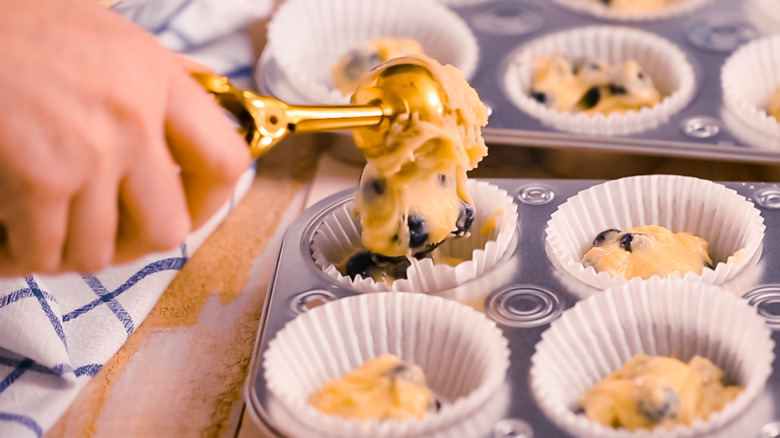 person scooping batter into muffin cup