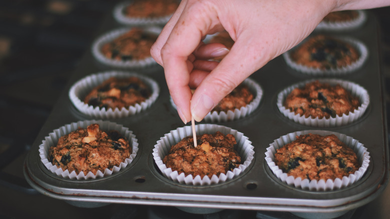 person inserting cocktail stick into muffin