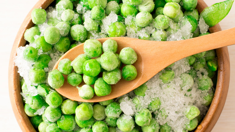 Icy frozen green peas in a bowl and on wooden spoon