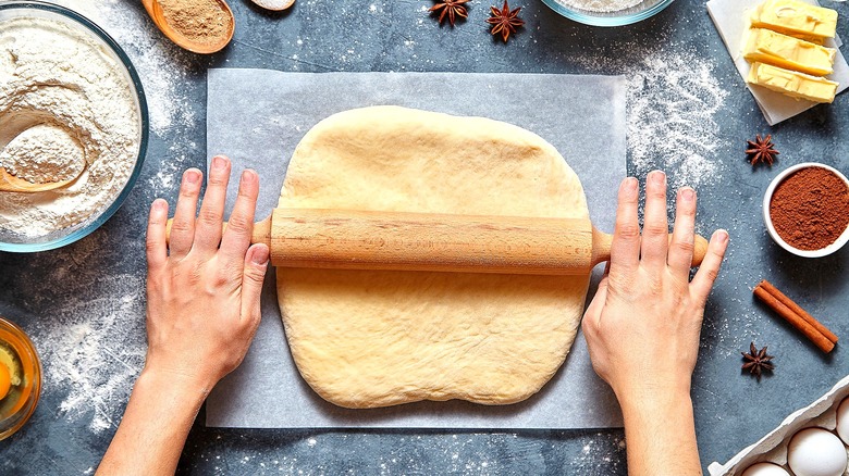 Hands rolling out pie crust on a white sheet of parchment paper