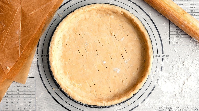 Unbaked pie crust in a tart pan next to parchment paper sheets and wooden rolling pin