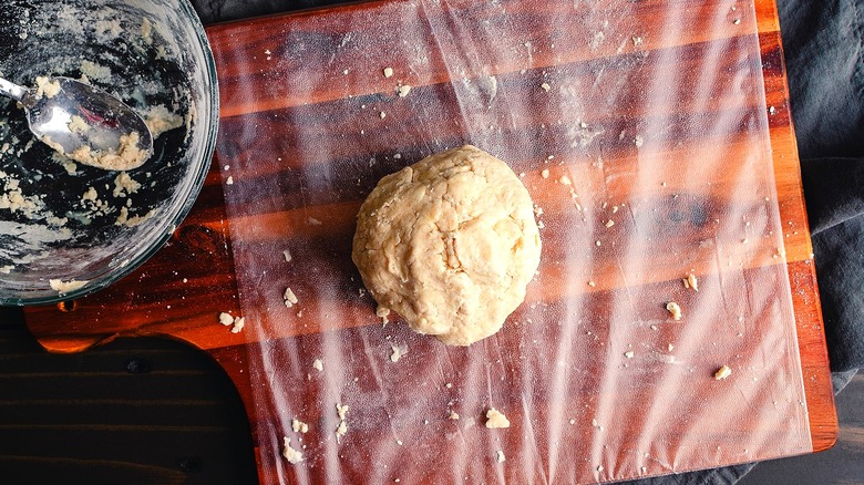 Ball of pie dough on a sheet of plastic wrap on a wooden cutting board