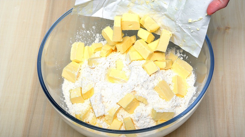 Cubed butter being added to a glass bowl of flour