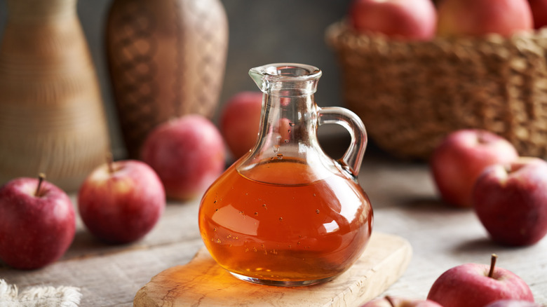 A bottle of apple cider vinegar and fresh apples.