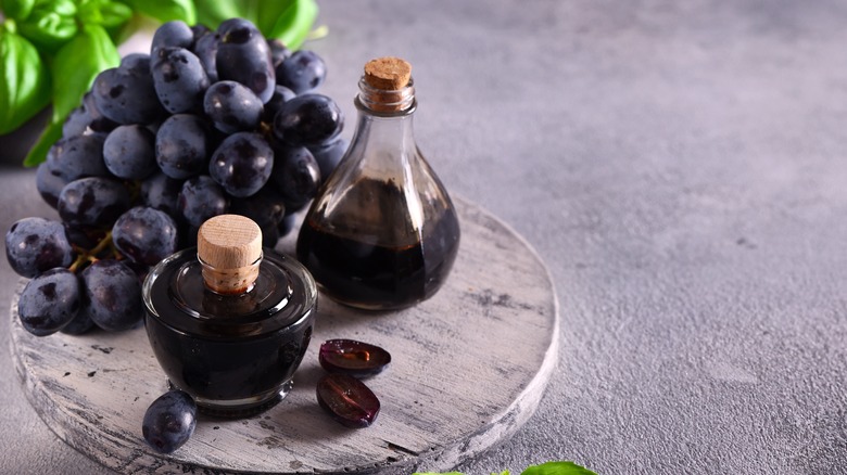 Two artisanal bottles of red wine vinegar next to a plate of concord grapes and fresh basil