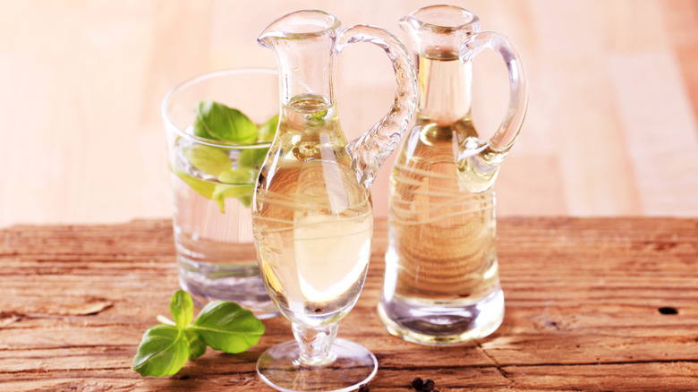 Bottles of white wine vinegar and oil with some fresh basil sit on a wooden table