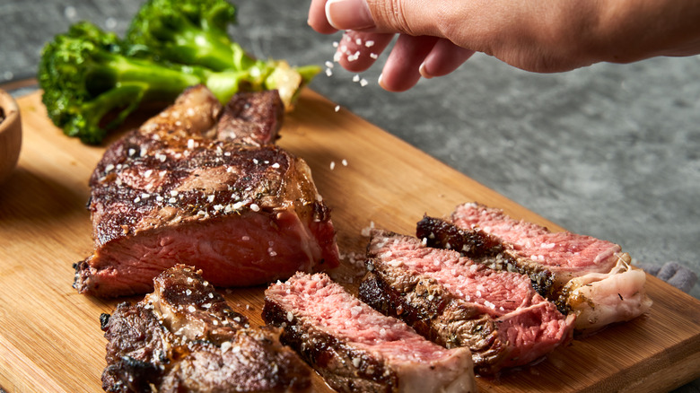 hand sprinkling coarse salt on cooked steak