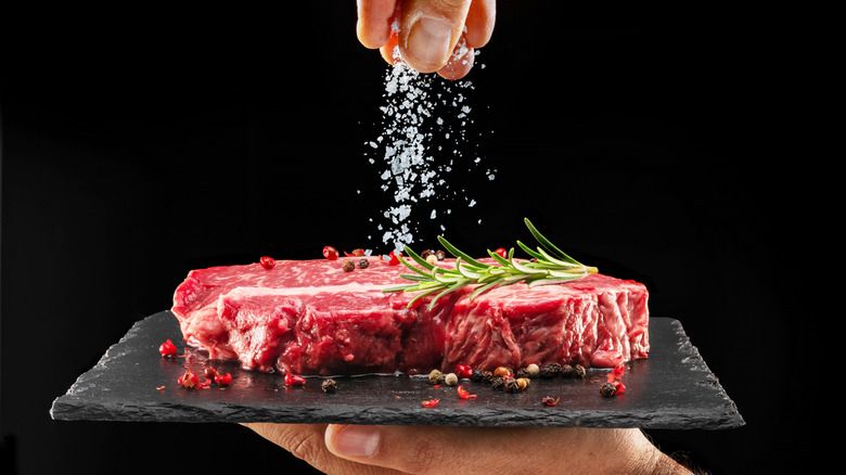 chef sprinkling salt over raw steak