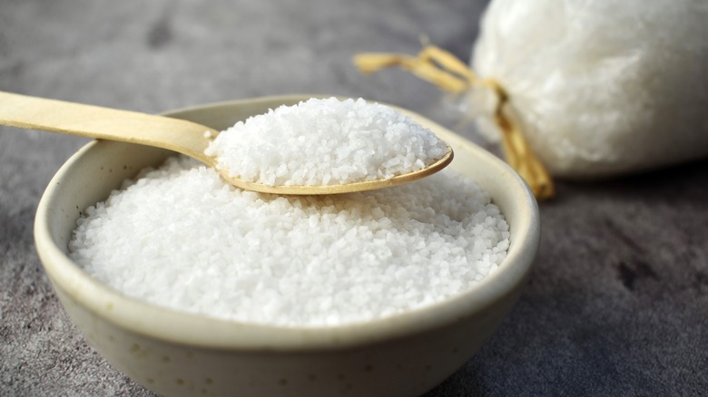 A wooden spoon scoops a helping of kosher salt from a white bowl