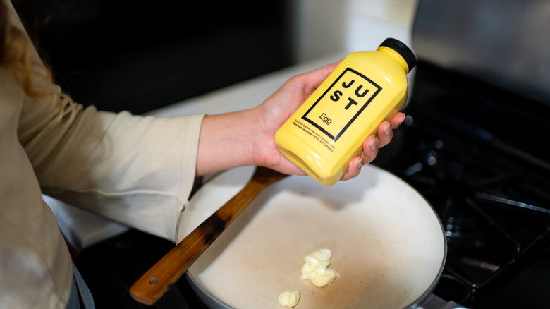 A home cook holds a bottle of vegan egg substitute over a frying pan