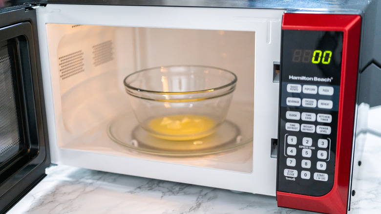 Melted butter sits in a glass bowl inside a red microwave with the door open