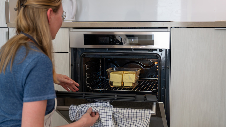 Woman places glass baking dish filled with butter into an oven