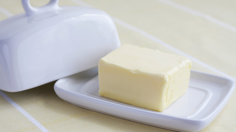 A partial stick of butter sits in a white ceramic dish on a countertop