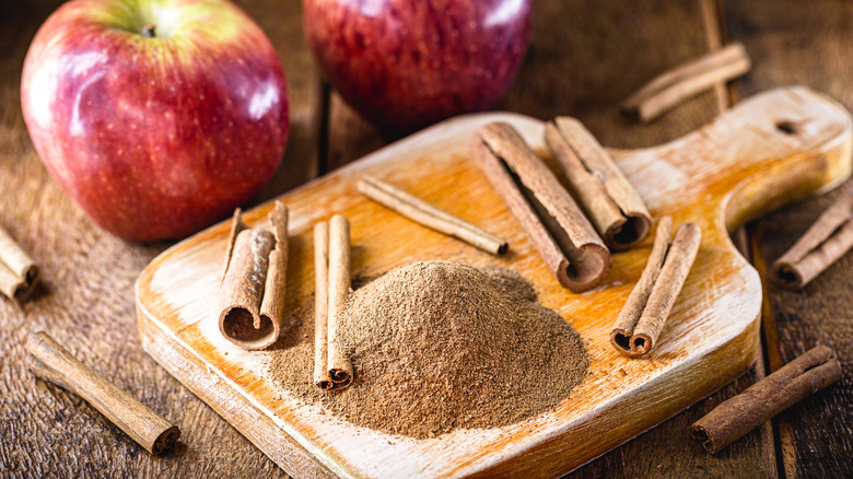 Cinnamon sticks and powder on wood cutting board with red apples