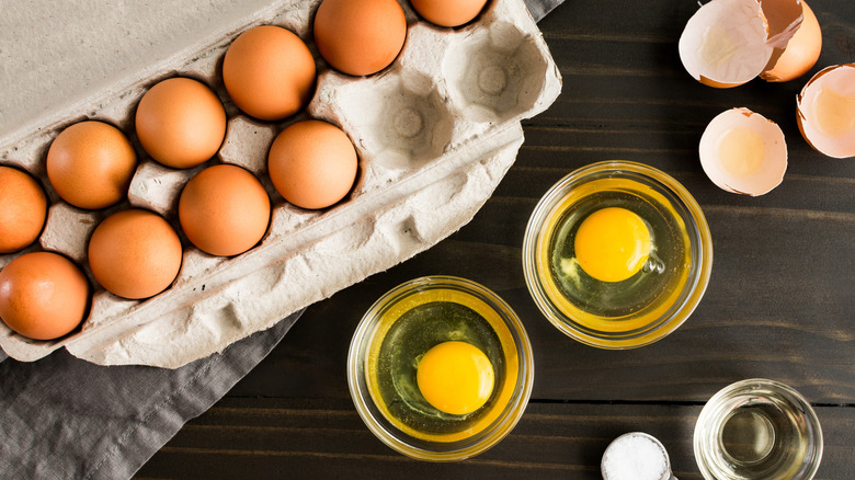 Cracked eggs in small glass bowl next to egg carton