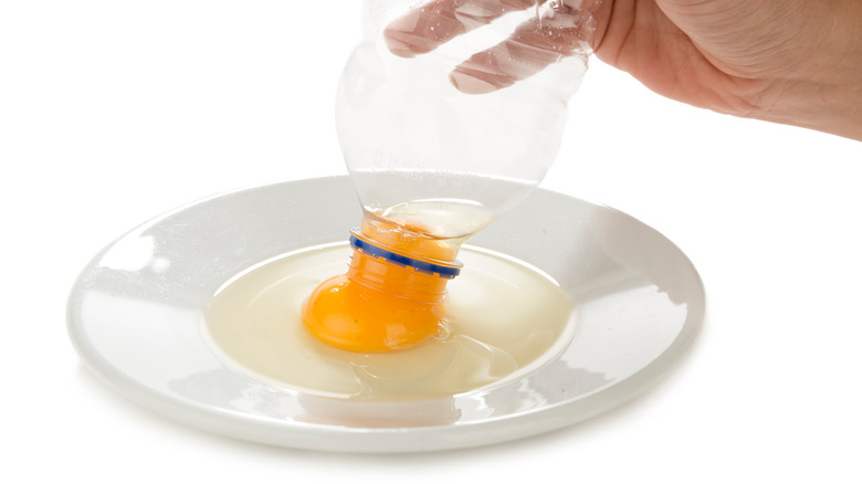 person touching an empty water bottle to egg yolk on plate