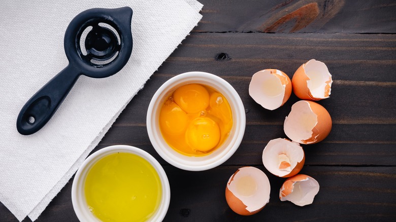 an egg separator alongside egg yolks and whites on wood surface