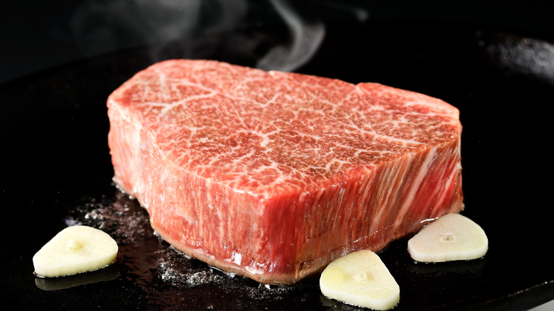 Wagyu steak cooking on black surface with garlic cloves