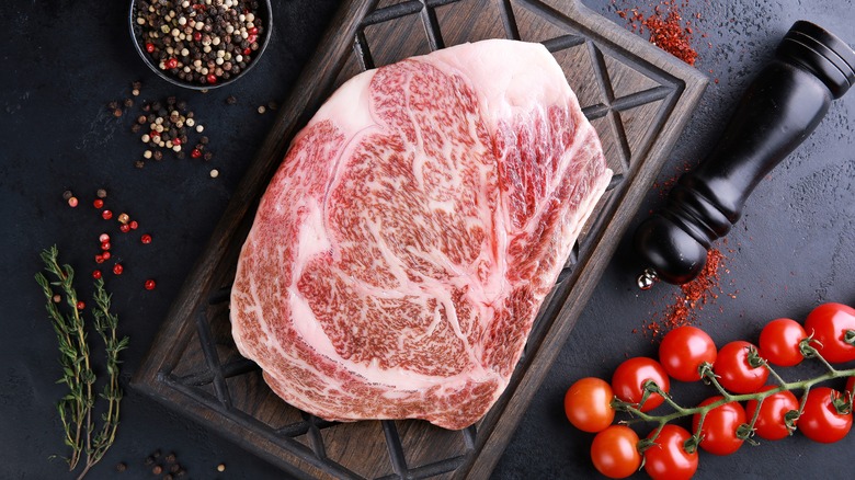 Raw Wagyu ribeye steak on a cutting board with tomatoes and seasonings